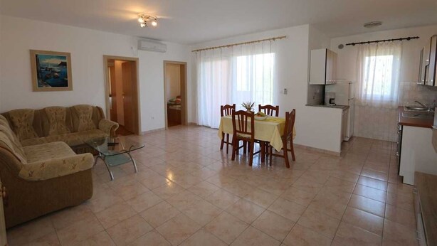 A living room with a sofa, a dining table with chairs, a kitchen area with cabinets and a sink, and a painting on the wall. - Apartment Dudovic Darko nr 3 (Silo - island Krk)