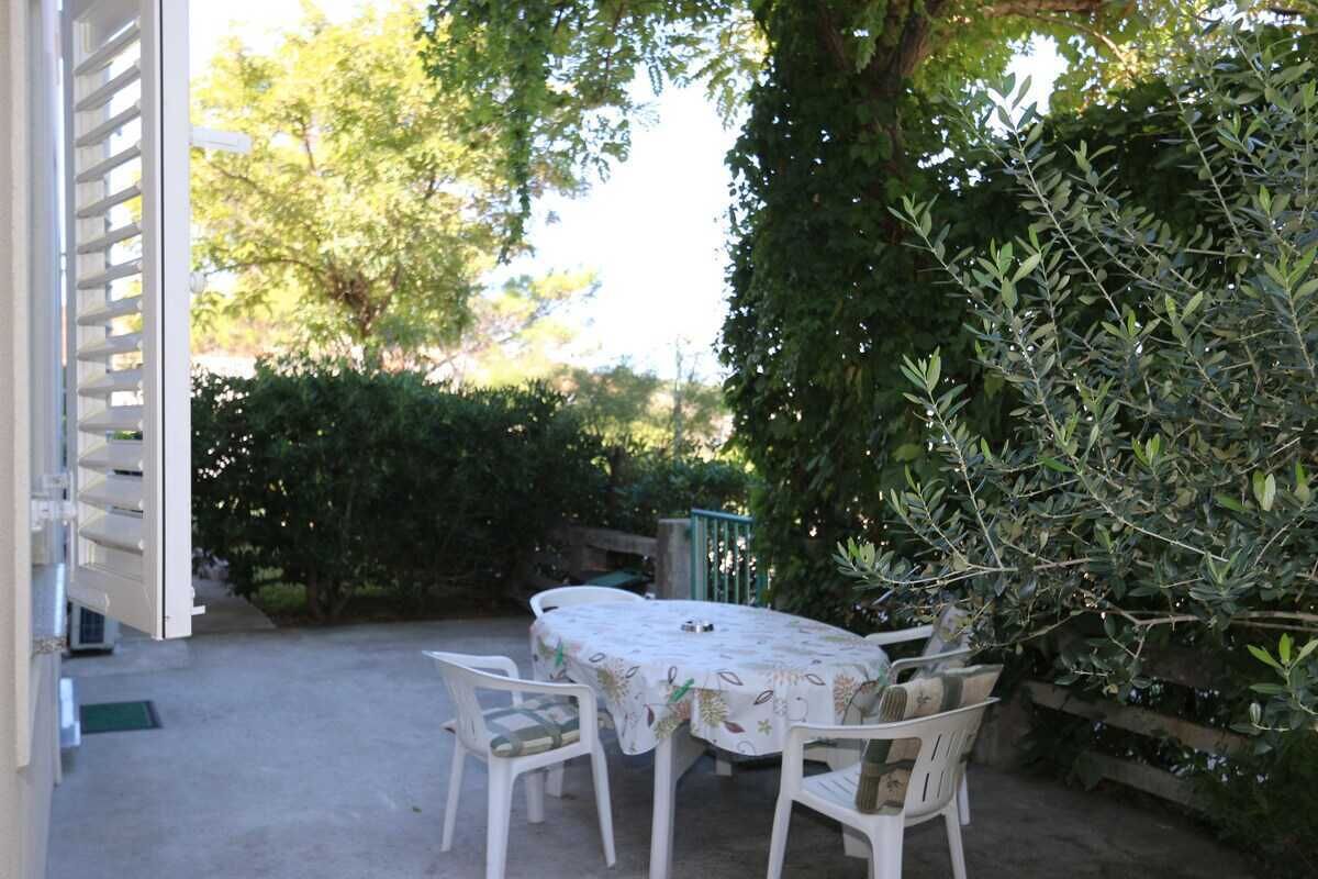 Un patio al aire libre con mesa y sillas, rodeado de vegetación y una cerca de madera.