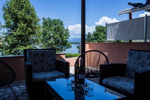 Un espace extérieur aménagé avec des meubles en osier, une table avec des verres et des bouteilles, et une vue sur un lac et des arbres.