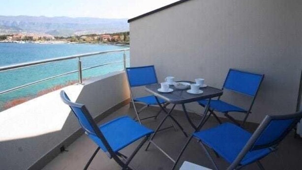 A balcony with a table and chairs, overlooking a body of water and distant mountains. - Apartment Djakovic Tihana 2 (Silo - island Krk)