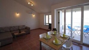 A living room with a sofa, a dining table set for two, and a balcony with blue chairs. - Apartment Djakovic Tihana 2 (Silo - island Krk)