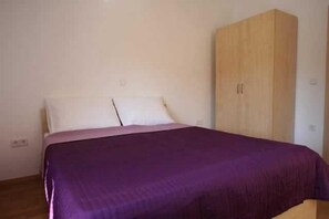 Un lit simple avec une couvre-lit violette, une armoire en bois et un mur blanc uni.
