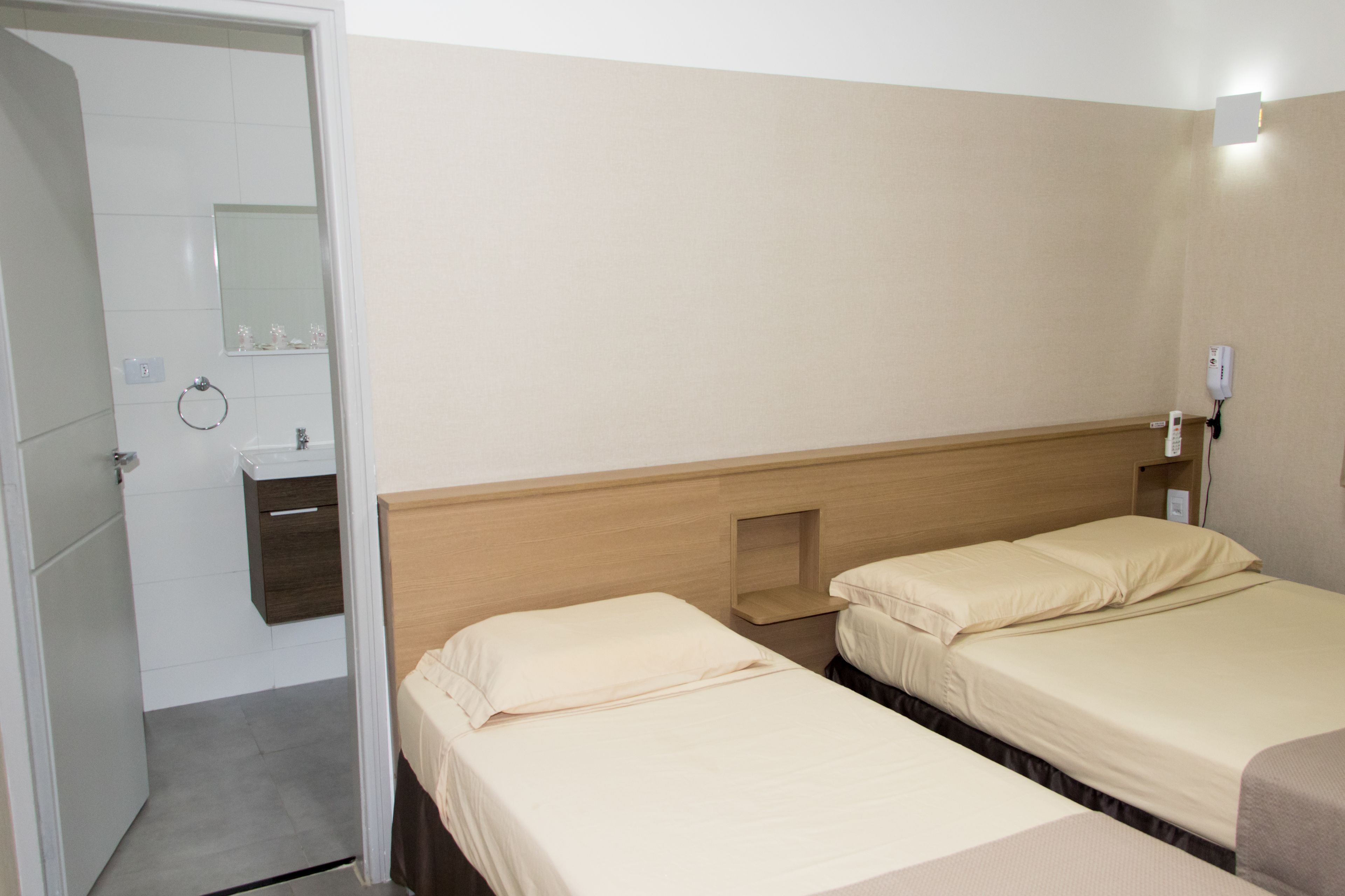 A hotel room with two beds, a wooden headboard, a small bedside table, a mirror, and a bathroom with a toilet and sink.