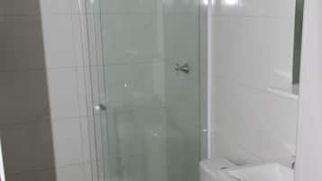 Un baño moderno con cabina de ducha de vidrio, inodoro blanco y tocador de madera con espejo.