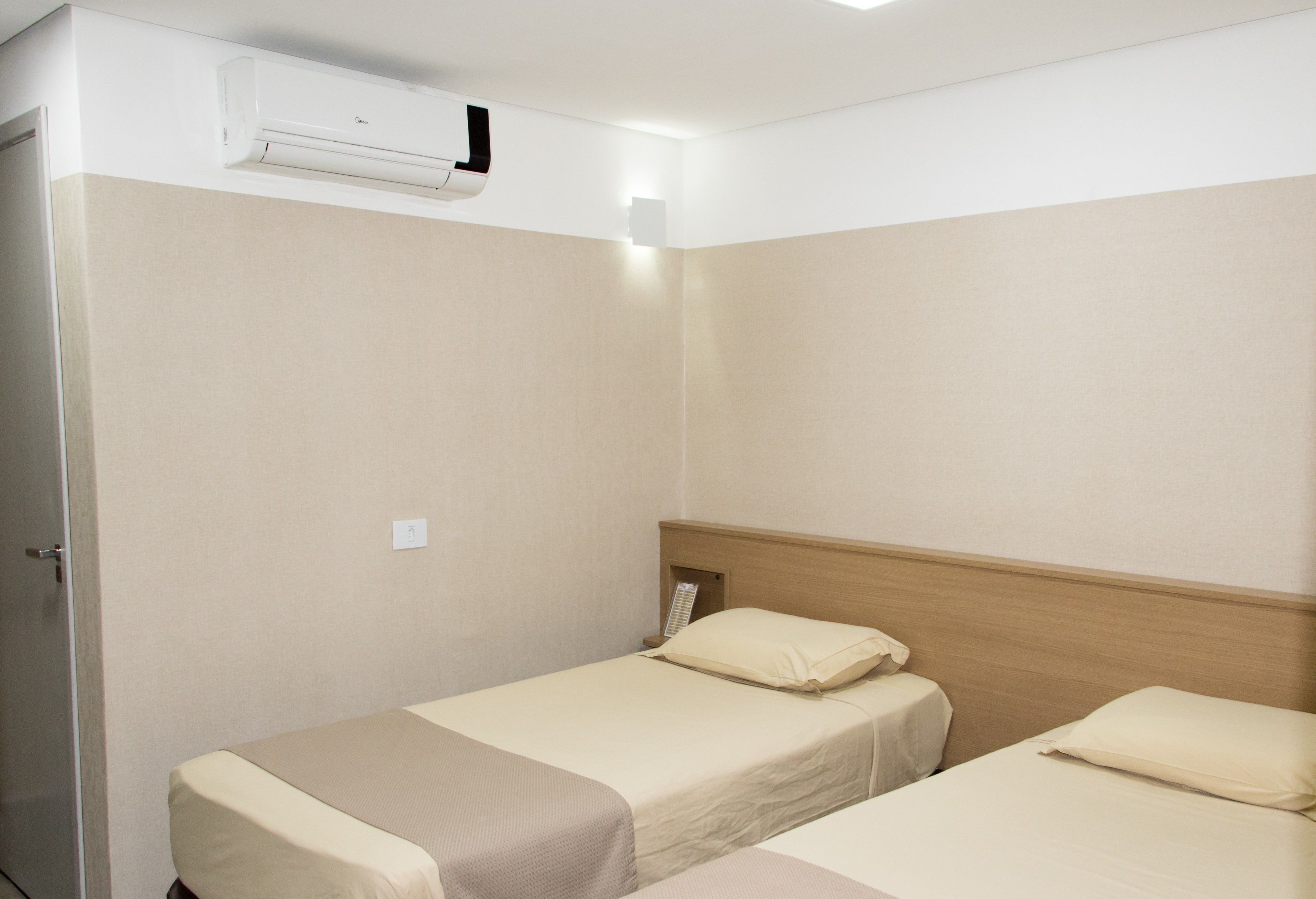 Une chambre d’hôtel avec deux lits simples, une tête de lit en bois, un climatiseur fixé au mur et une porte située sur le côté gauche.