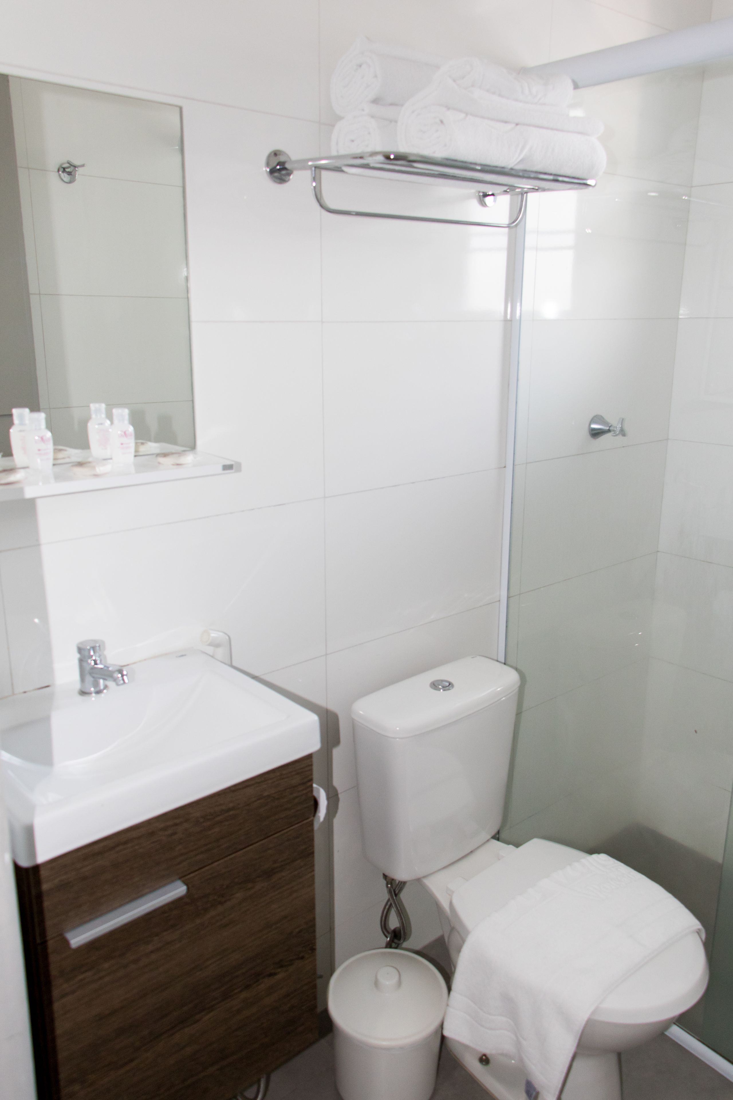 Ein modernes Badezimmer mit einem weißen Waschbecken, einem Spiegel, einer Duschkabine aus Glas und einer Toilette.