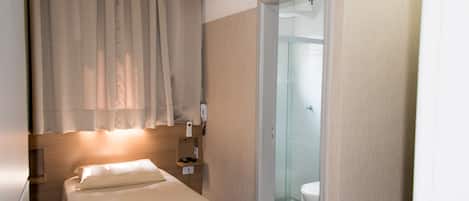 Habitación de hotel con cama, mesita de noche, teléfono y baño visible a través de una puerta de cristal.