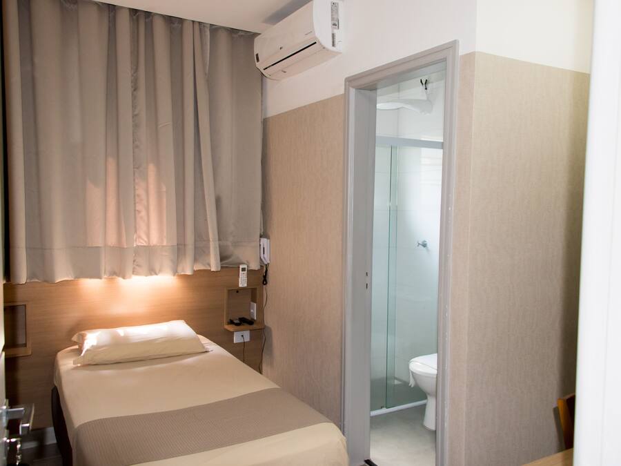 Ein Hotelzimmer mit Bett, Nachttisch, Telefon und einem durch eine Glastür einsehbaren Badezimmer.