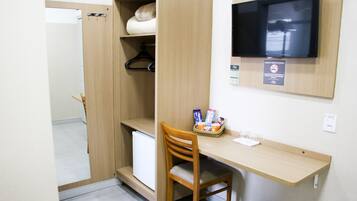 A compact room with a wooden desk, a chair, a television mounted on the wall, and a small refrigerator.