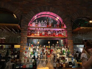 A bar area with a brick archway, shelves of various liquor bottles, and glasses.
