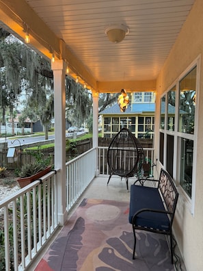 A covered porch with a bench and a chair, a decorative light fixture, and a view of a house with a blue roof.