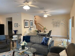 A modern living room with a sofa, coffee table, and ceiling fans. There is a staircase leading to another level.