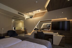 A modern hotel room with a large bed, a desk with a computer, a TV, and a mirror.