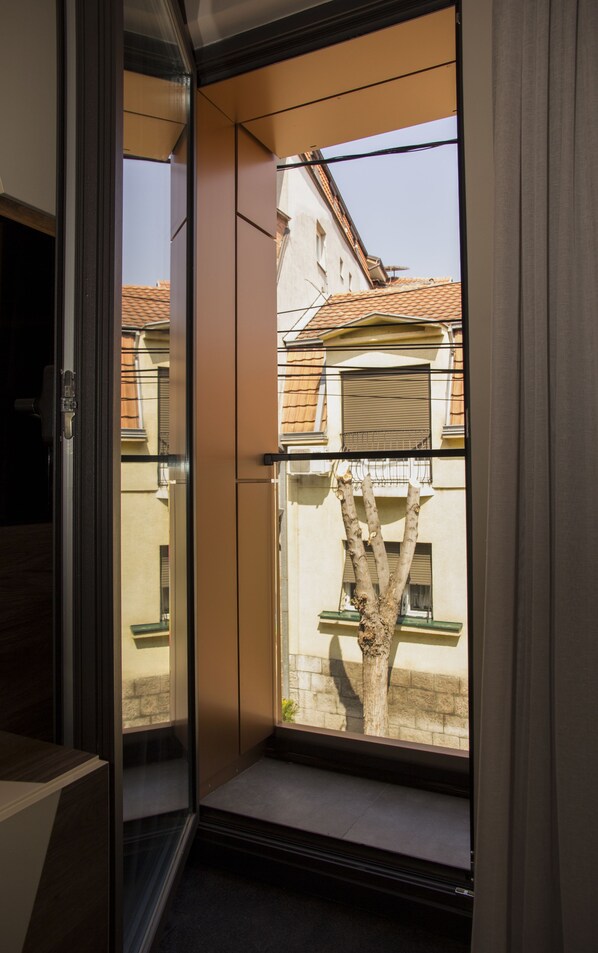 A room with a sliding glass door leading to a balcony with a view of a tree and buildings.