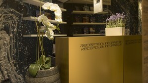 A reception desk with a modern design, including a large vase with white orchids, a gold reception area, and a marble wall with a black and white pattern. - Garni Hotel Boutique 25h (Niš)