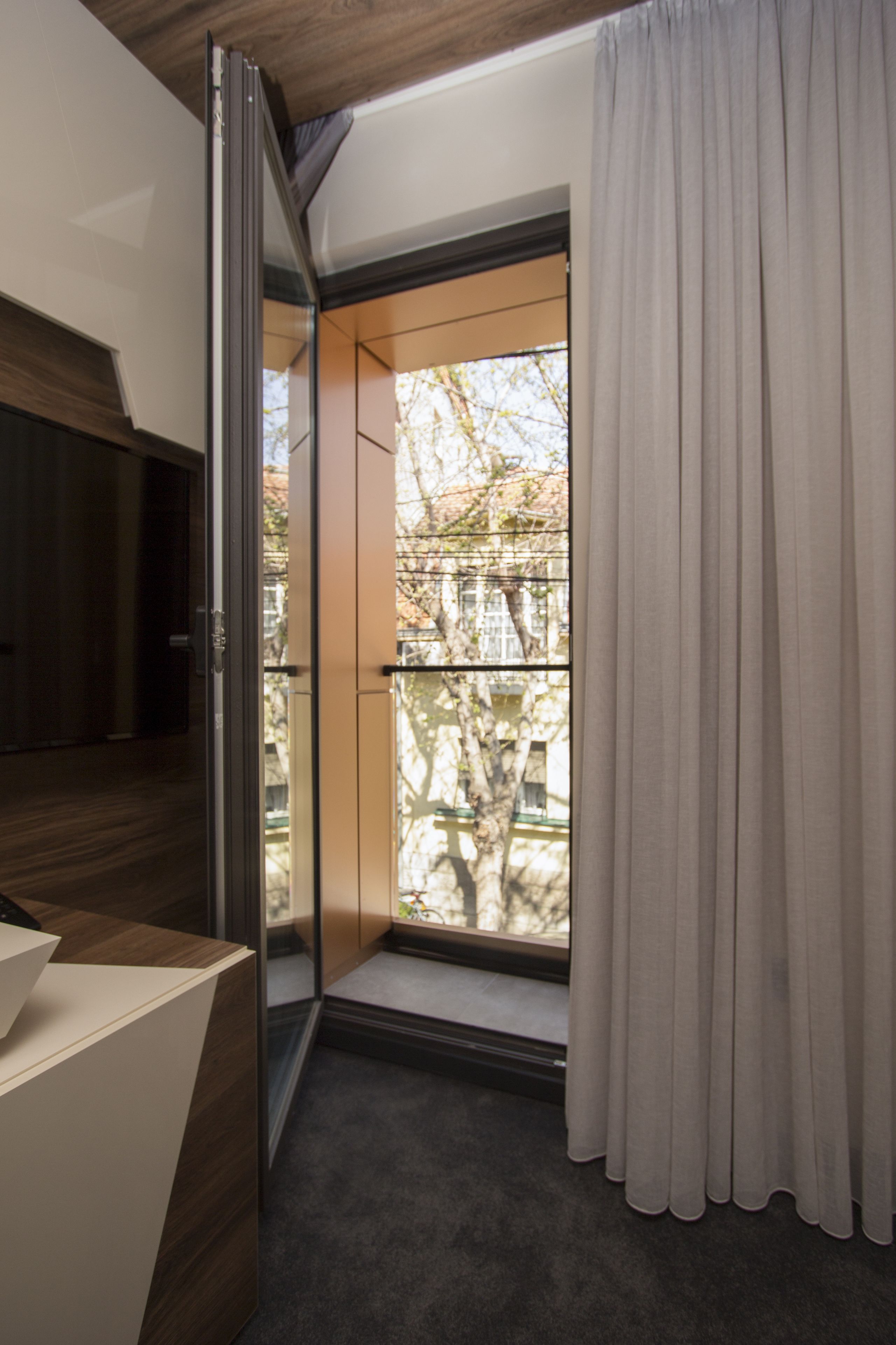A modern room with a sliding glass door leading to a balcony, a wooden desk, and a window with curtains.