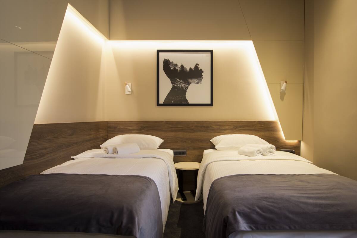 A hotel room with two beds, a round table, and a framed artwork on the wall.