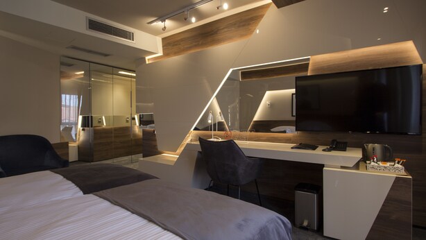 A modern hotel room with a large bed, a desk with a flat-screen TV, and a seating area. - Garni Hotel Boutique 25h (Niš)