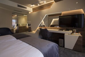 A modern hotel room with a large bed, a desk with a flat-screen TV, and a seating area.