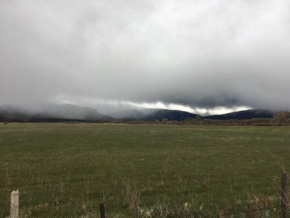 Un campo extenso con una cerca de madera en primer plano y una cadena montañosa al fondo bajo un cielo nublado.