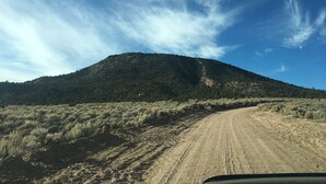 A dirt road winding through a hilly landscape with sparse vegetation and a clear blue sky. - Hike By Light, Campers Delight. (Fort Garland)
