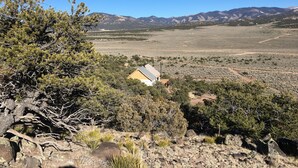 A remote cabin in a mountainous area with sparse vegetation and a clear sky. - Hike By Light, Campers Delight. (Fort Garland)