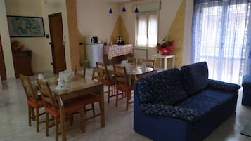 Un comedor con una mesa dispuesta para cuatro personas, un sofá y una cocina equipada con refrigerador y microondas.