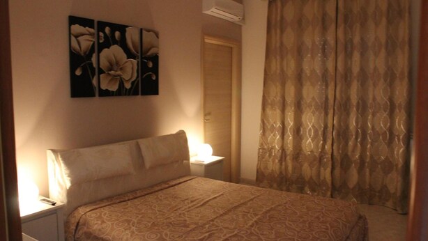 A bedroom with a bed, a nightstand, a wall-mounted air conditioner, and a curtain. - Bethel Bed and Breakfast (Gela)