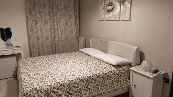 Una cama bien hecha con una colcha estampada, una mesita de noche con una lámpara y una pared decorada con motivos florales.