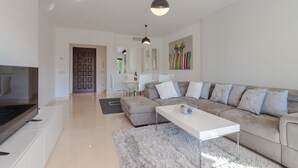 A modern living room with a sectional sofa, a flat-screen TV, and a dining area with a white table and chairs. - Prime location within beautiful gated community - LATE AVAILABILITY! (Benahavís)