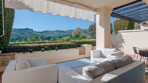 A covered outdoor seating area with wicker furniture and a view of the hills. - Prime location within beautiful gated community - LATE AVAILABILITY! (Benahavís)