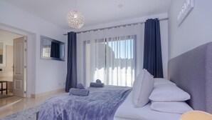A bedroom with a large bed, a flat-screen TV, and a modern chandelier. - Prime location within beautiful gated community - LATE AVAILABILITY! (Benahavís)