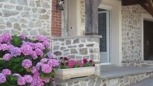 Ein Steinhaus mit einer Steinaußenwand, einem Holzbalkengerüst und einem Blumenbeet mit rosa Blüten.