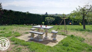 Ein Garten mit einem Steintisch und Bänken, umgeben von Gras und einer Hecke.