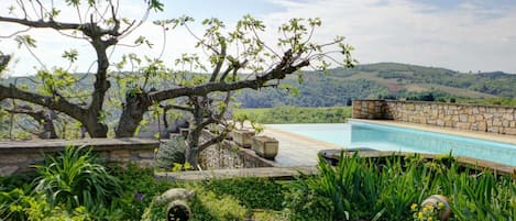 Un área de piscina con muro de piedra, abundante vegetación y vistas a las colinas.
