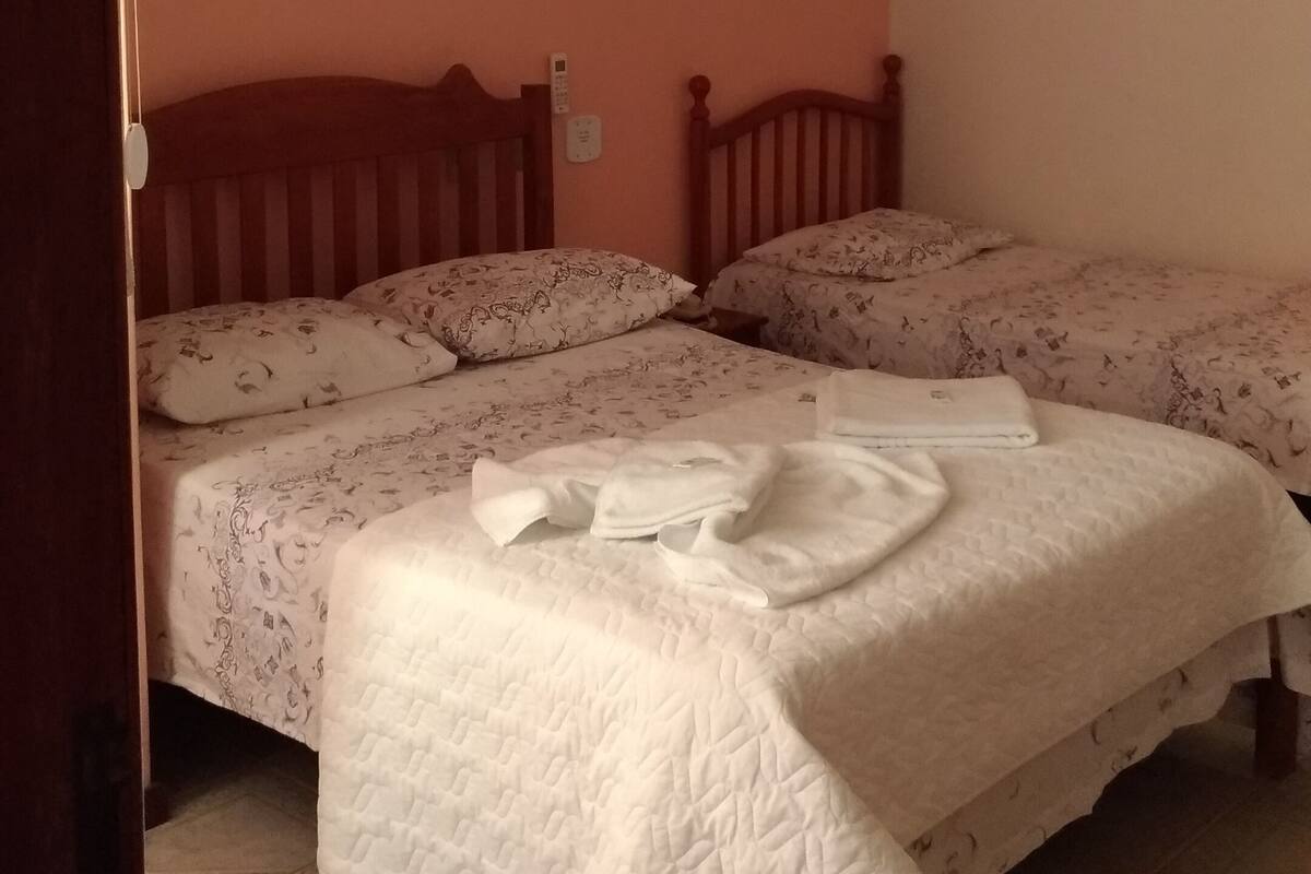 Quarto com duas camas, cabeceira de madeira, mesa de cabeceira e telefone fixado na parede.
