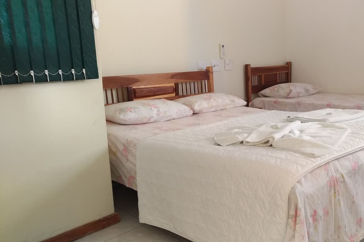 Quarto de hotel com duas camas de solteiro, cada uma com roupa de cama floral e cabeceiras de madeira. Há toalhas nas camas e um termostato na parede.