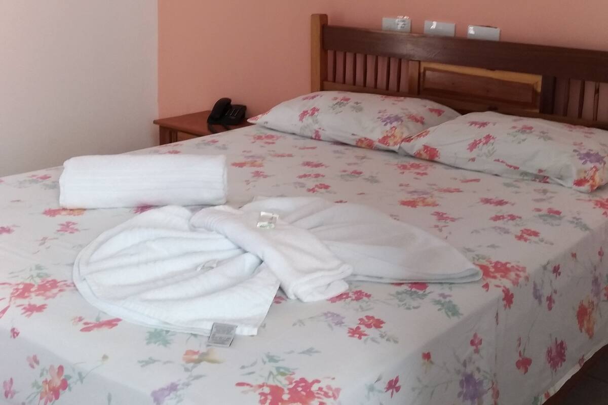Cama bem arrumada com roupa de cama floral, cabeceira de madeira e um quadro na parede.