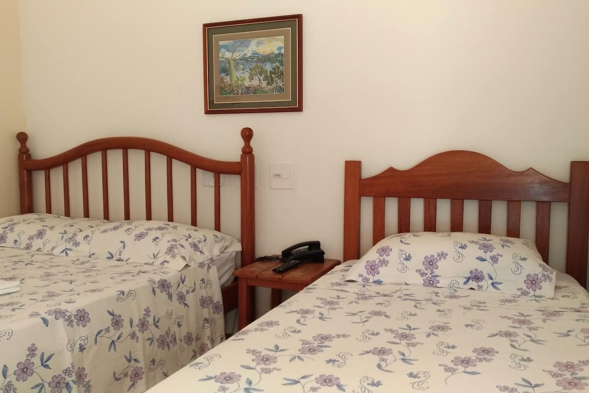 Quarto com duas camas de madeira, cada uma com roupa de cama floral. Há um quadro na parede acima das camas.