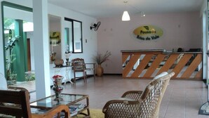 Un área de recepción con muebles de mimbre, una mesa de vidrio y un letrero que dice "Pousada Brisa do Vale".