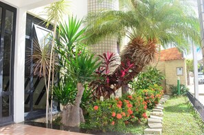 A modern building with a glass entrance, surrounded by various tropical plants and a stone pathway. - Pousada Brisa do Vale (Itaobim)