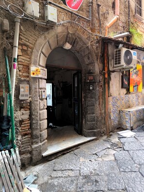 An entrance to a building with a stone archway, a sign indicating room number 20, and an air conditioning unit on the right. - Small loft in the heart of the Spanish neighborhoods (Napoli)