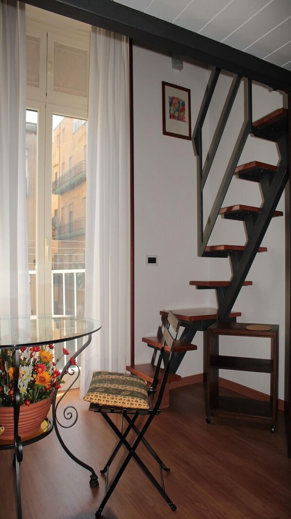 A room with a glass table, a chair, a potted plant, and a wooden staircase. - Small loft in the heart of the Spanish neighborhoods (Napoli)
