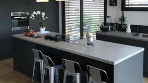 Cocina moderna con una isla central, taburetes de bar, iluminación colgante y vistas a zonas verdes por la ventana.