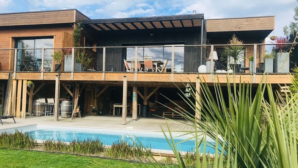 Una casa moderna con piscina, terraza de madera y zona de estar exterior.