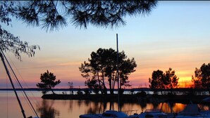 Un puerto deportivo con barcos amarrados, un lago tranquilo y árboles silueteados contra el cielo al atardecer.