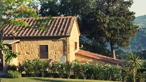 Uma casa de pedra com telhado de telhas, rodeada por vegetação exuberante e árvores.