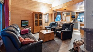 Accogliente interno di una baita con soffitto in legno, una zona living con divani in pelle, un mobiletto in legno e un camino.