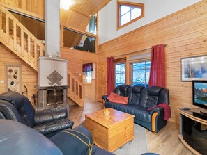 A cozy cabin interior with a fireplace, leather sofas, a wooden coffee table, and a television.