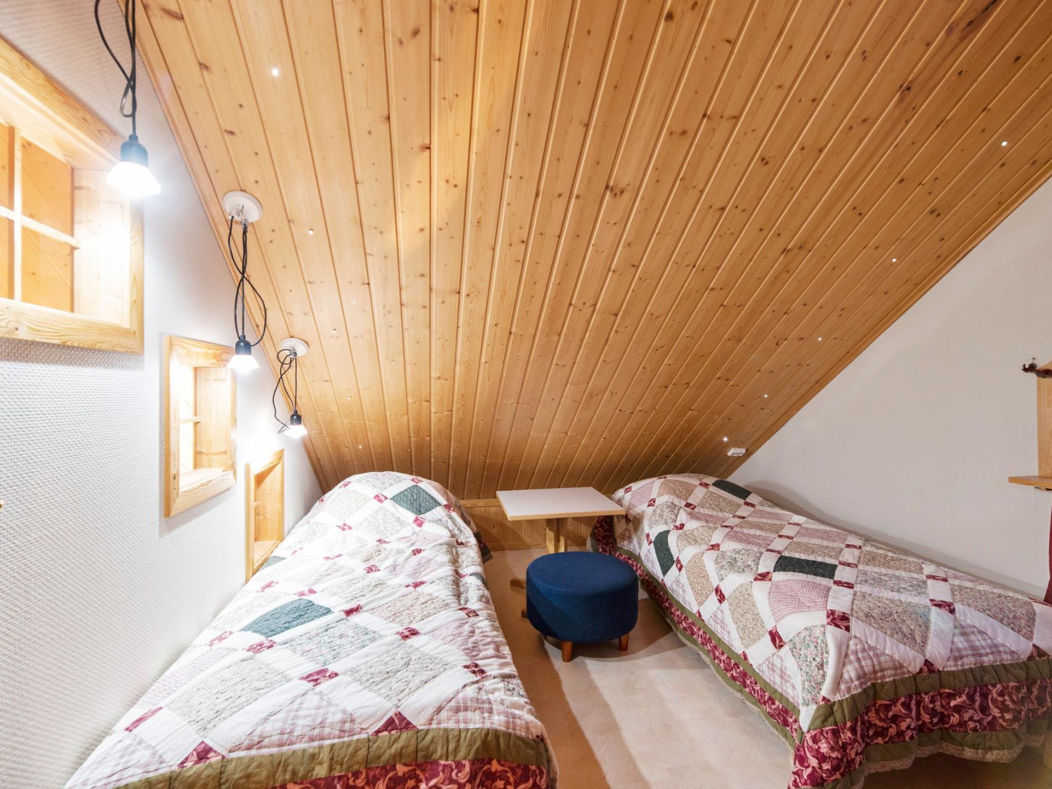 Un dormitorio ático acogedor con dos camas individuales, una mesita y un banco.